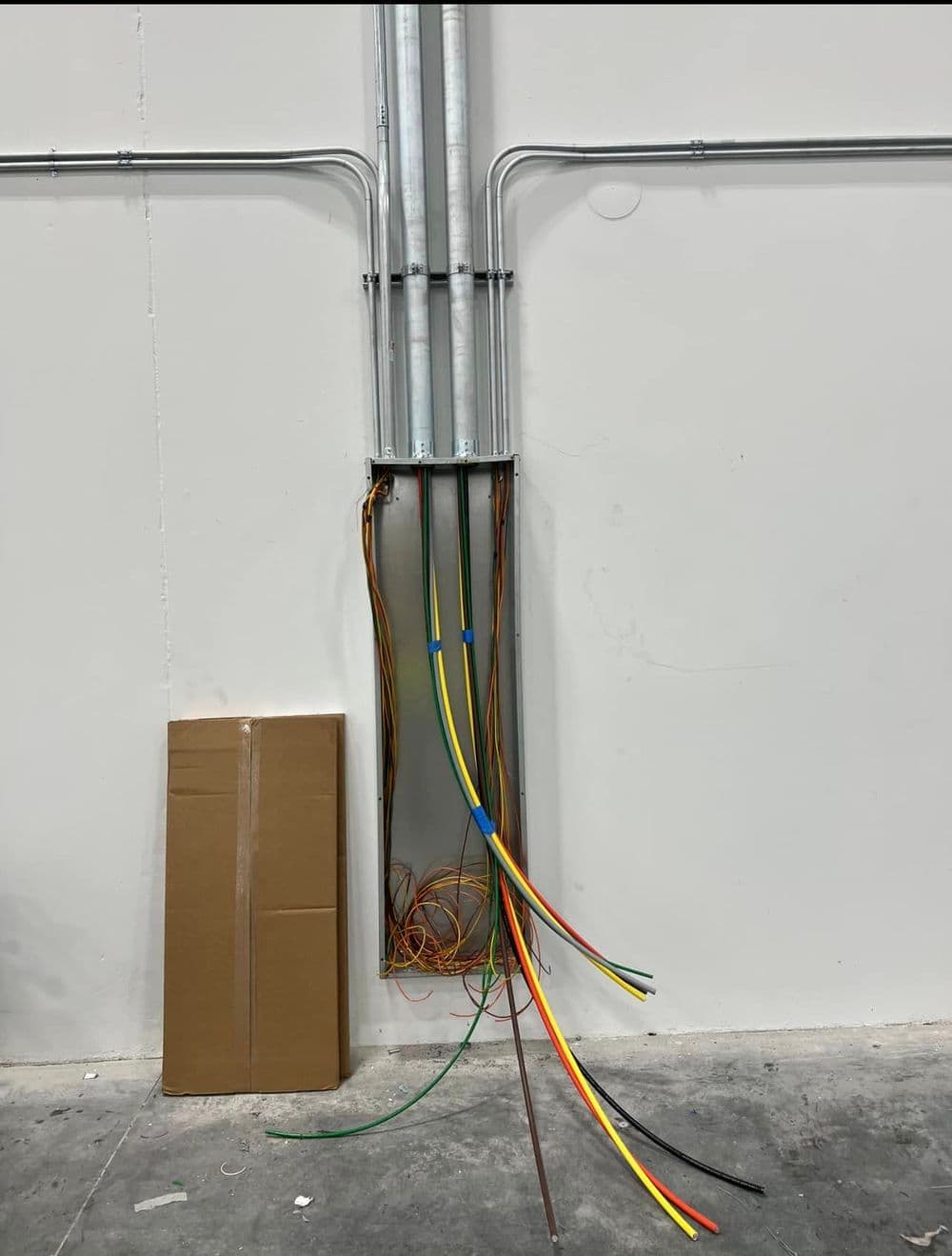 Electrical conduit with exposed colorful wiring next to a cardboard box in an industrial setting.