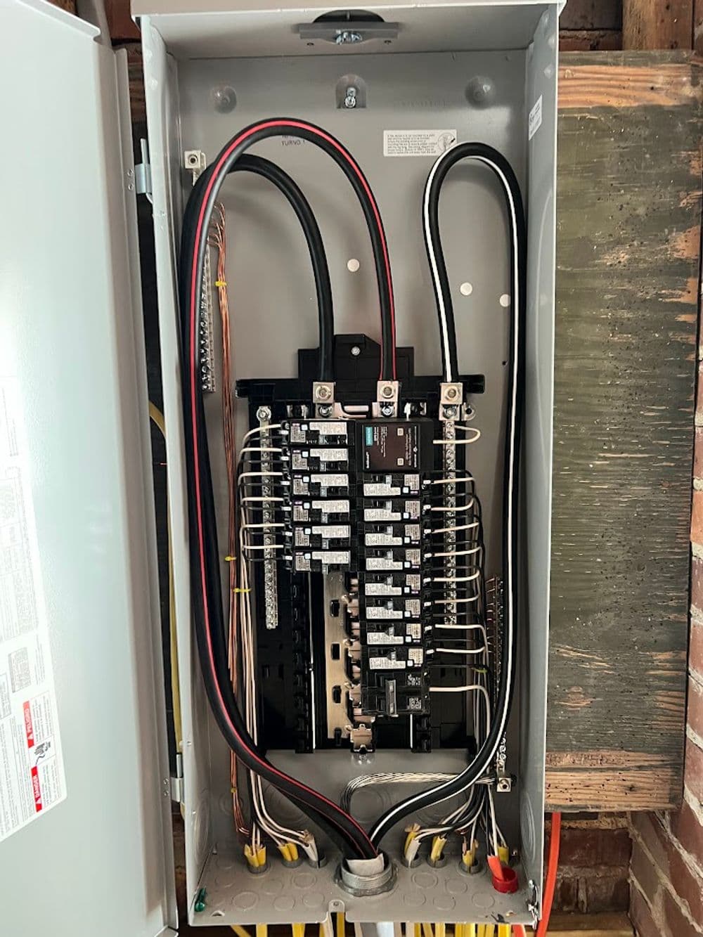 Electrical panel with circuit breakers and wiring, installed in a home setup.