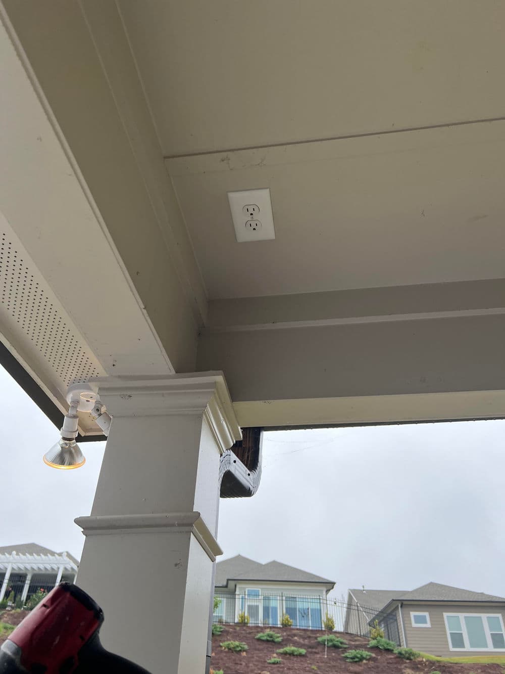 Electrical outlet on ceiling under patio, with residential homes in background.