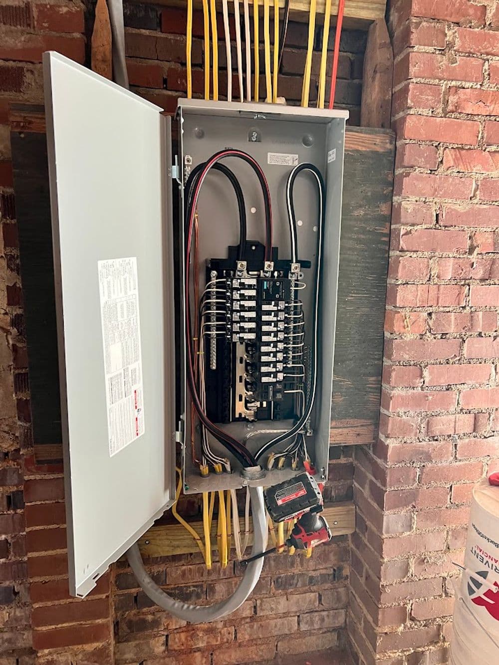 Electrical panel with circuit breakers and wiring in a brick wall installation.