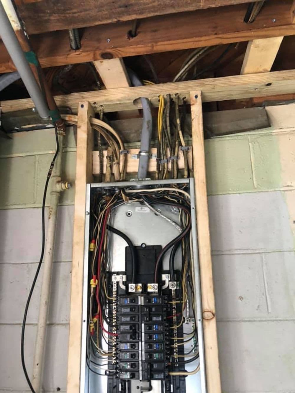 Electrical panel with circuit breakers and wiring in a basement setting.