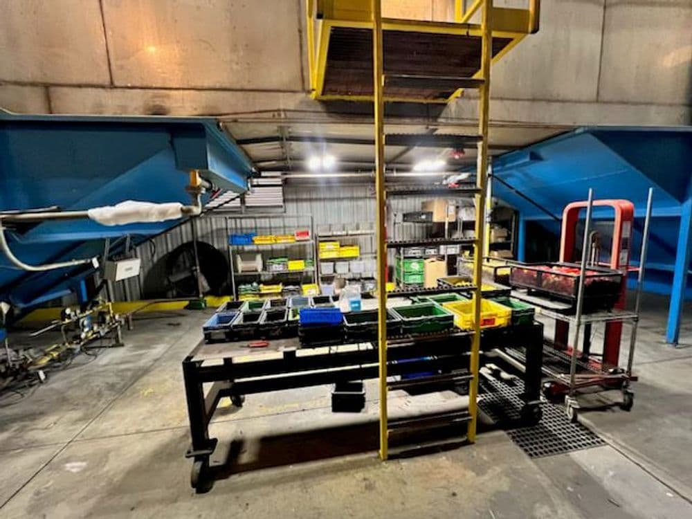 Industrial workspace with sorting tables, storage bins, and yellow ladder in a facility.