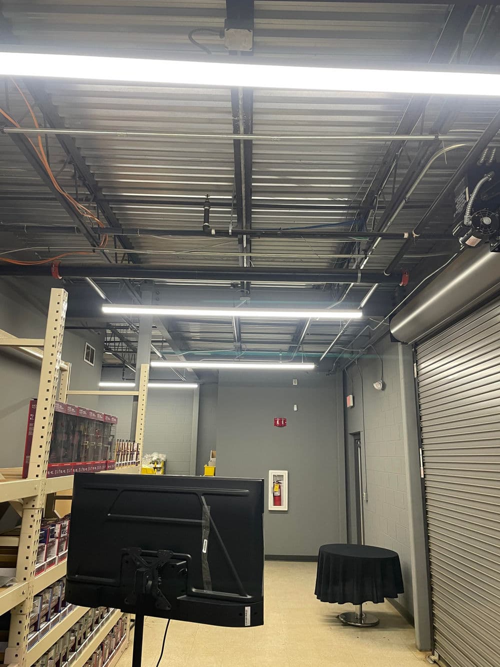 Brightly lit warehouse interior with shelving, monitor, and black table.