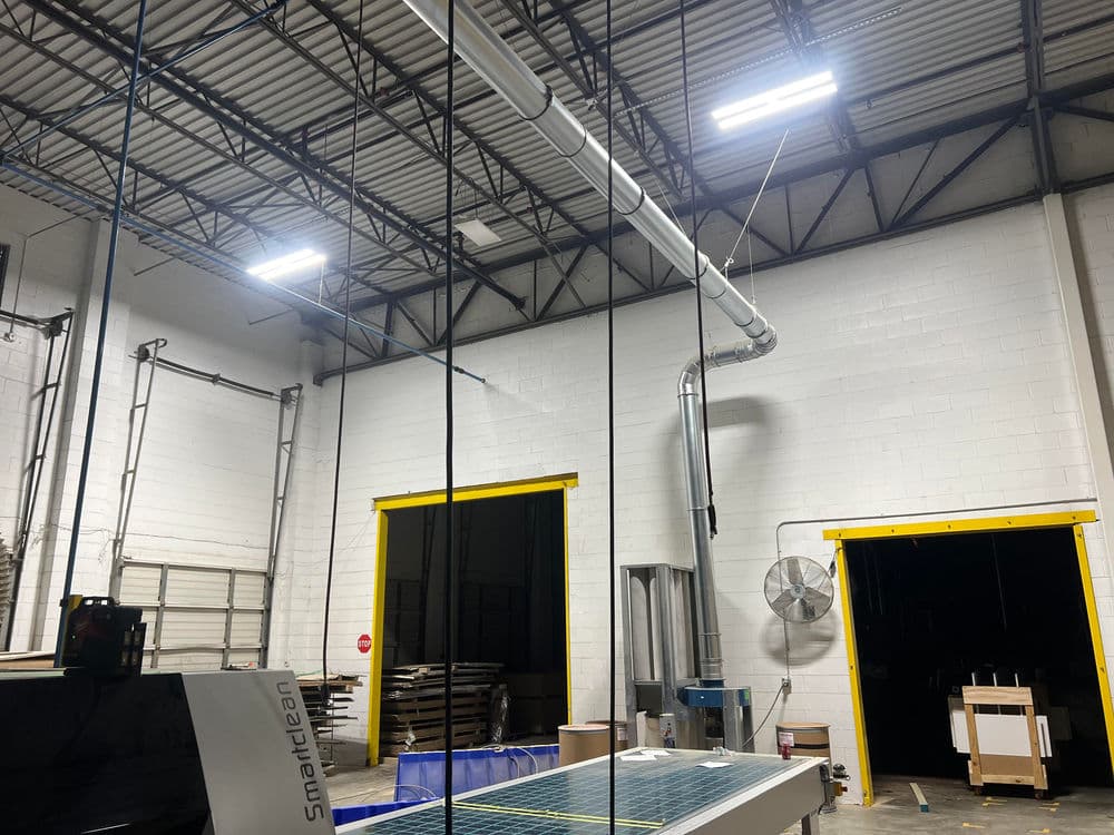 Industrial warehouse interior with overhead ventilation, LED lights, and cutting machinery.