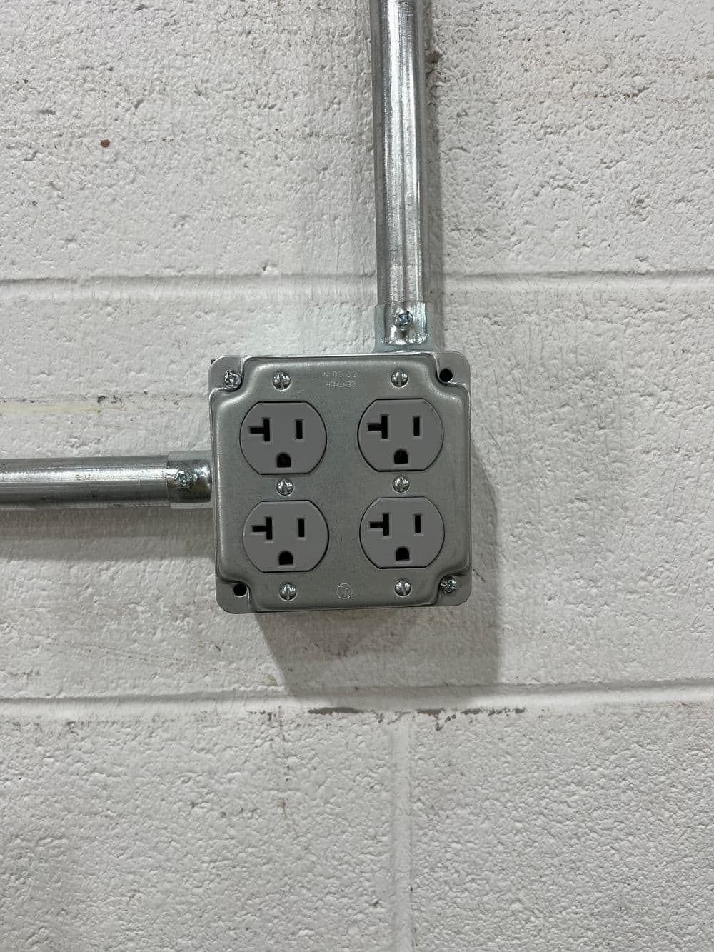 Electrical outlet with four sockets mounted on a gray concrete wall.