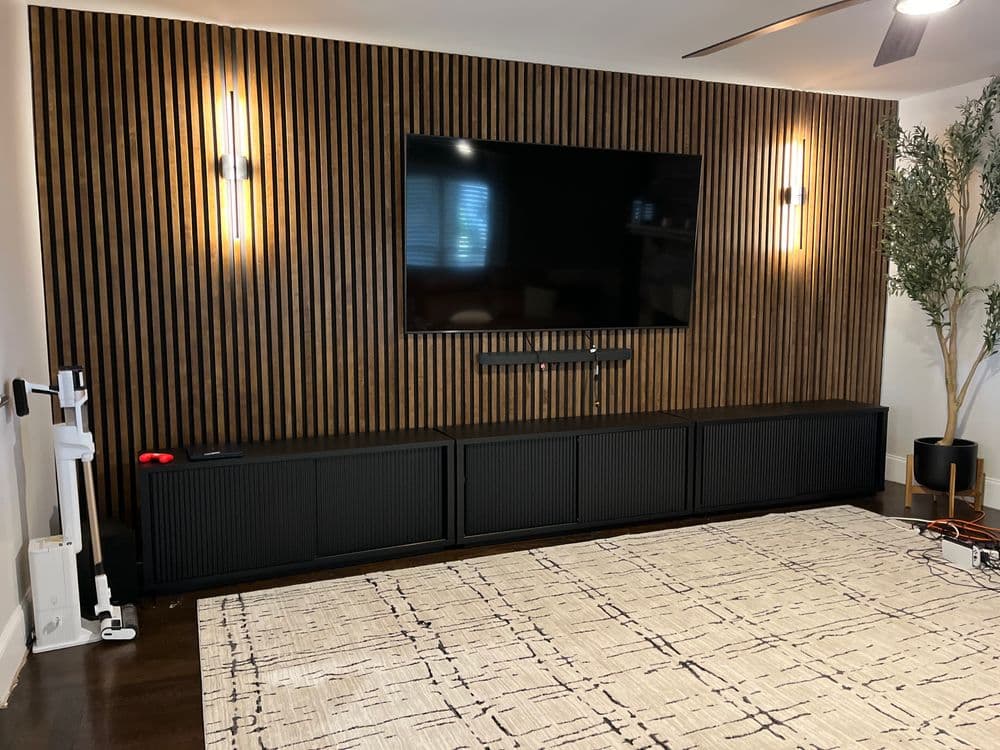 Modern living room with wooden accent wall, flat-screen TV, dark media console, and stylish decor.