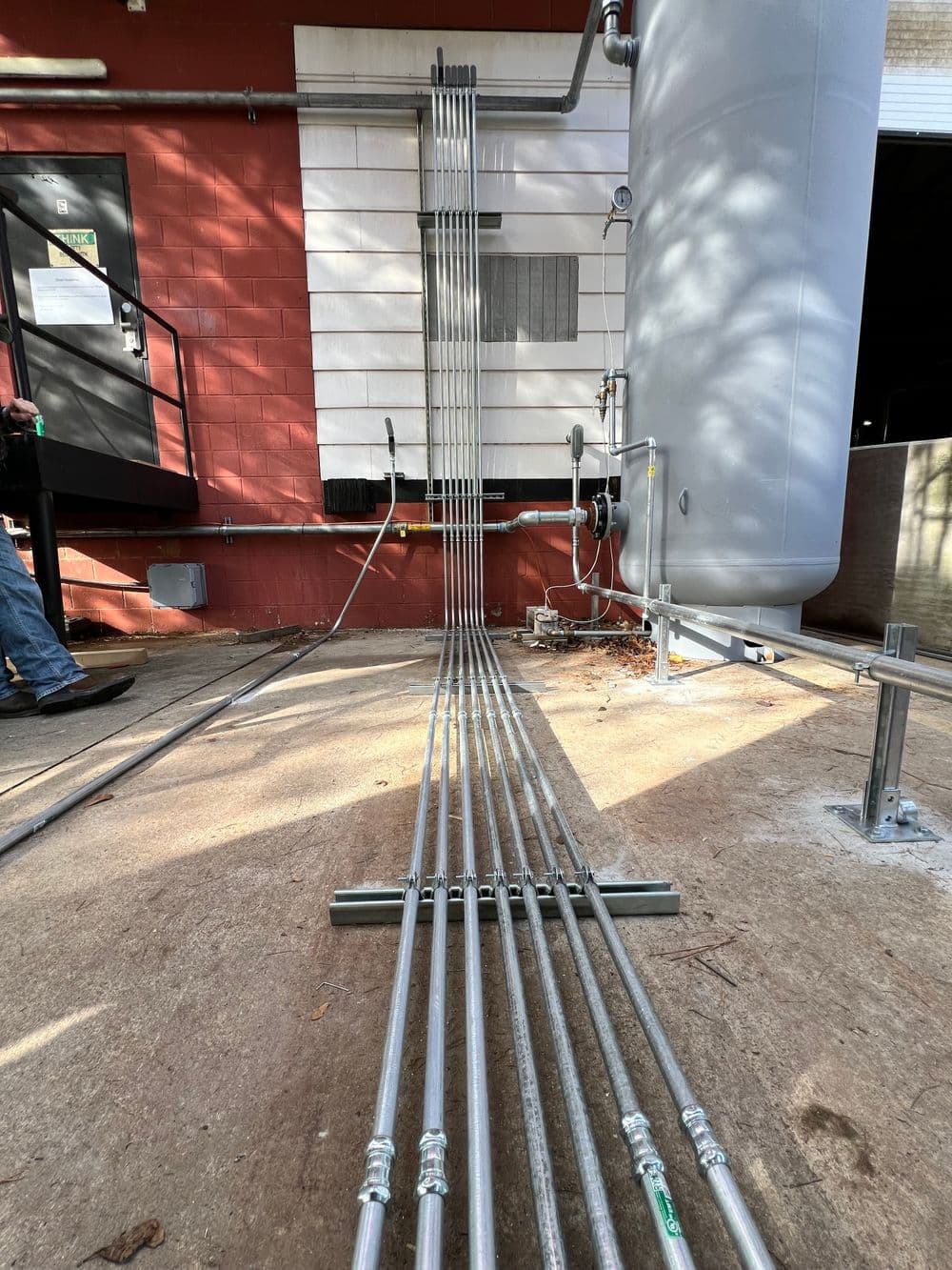 Metal piping installation leading to a large water heater outside a building.