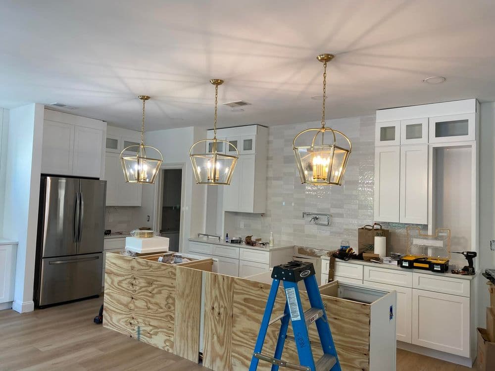 Modern kitchen with white cabinets, gold pendant lights, and wooden island under construction.