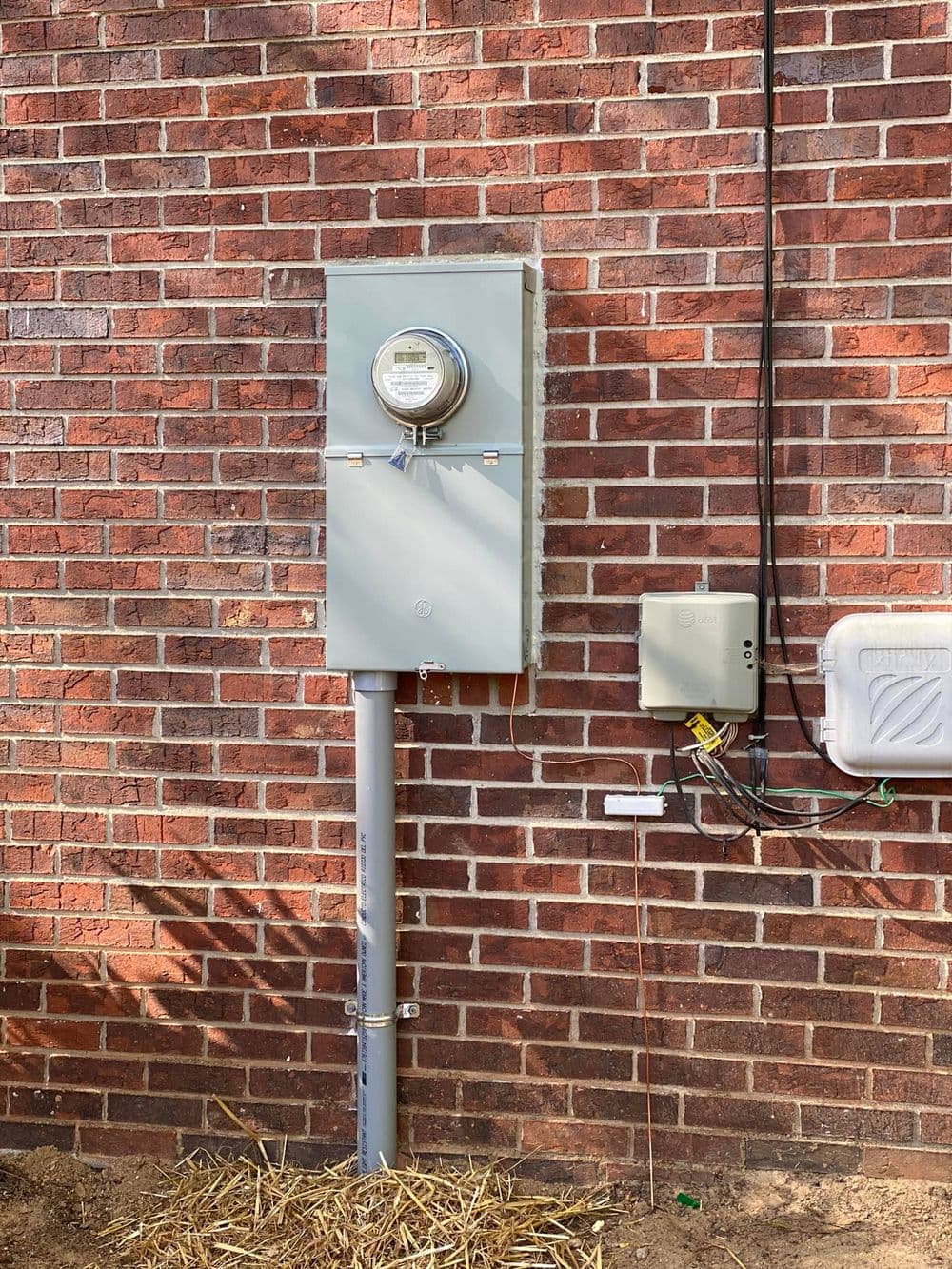 Electric meter mounted on brick wall with adjacent service panel and wiring details.