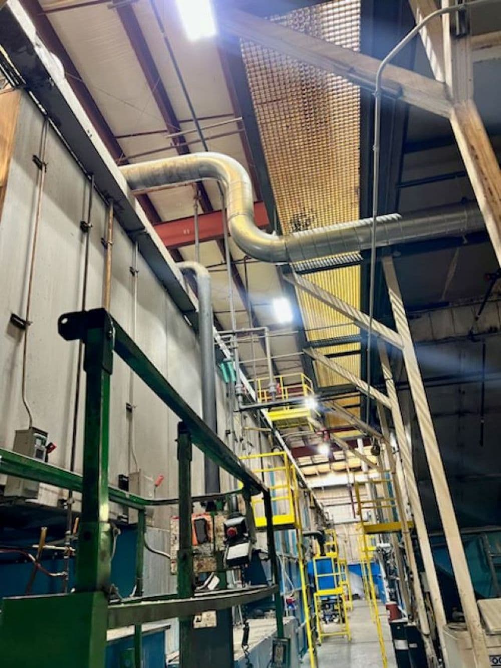 Industrial interior showing machinery, ductwork, and safety stairs in a manufacturing facility.