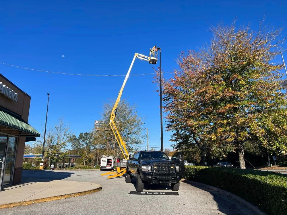 Worker on cherry picker repairing power lines near a black truck under a clear blue sky.