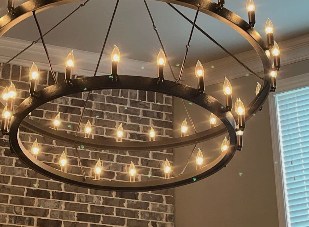 Chandelier with multiple light bulbs hanging against a brick wall. Elegant home lighting decor.