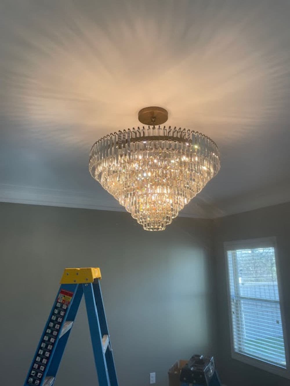 Modern crystal chandelier illuminating a room, above a ladder for installation.