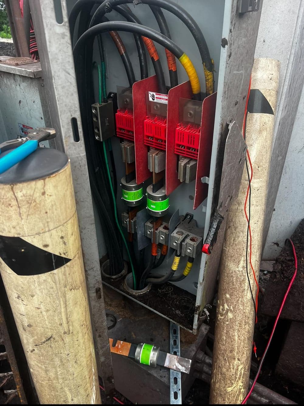 Electrical panel with fuses and high-voltage connections in industrial setting.