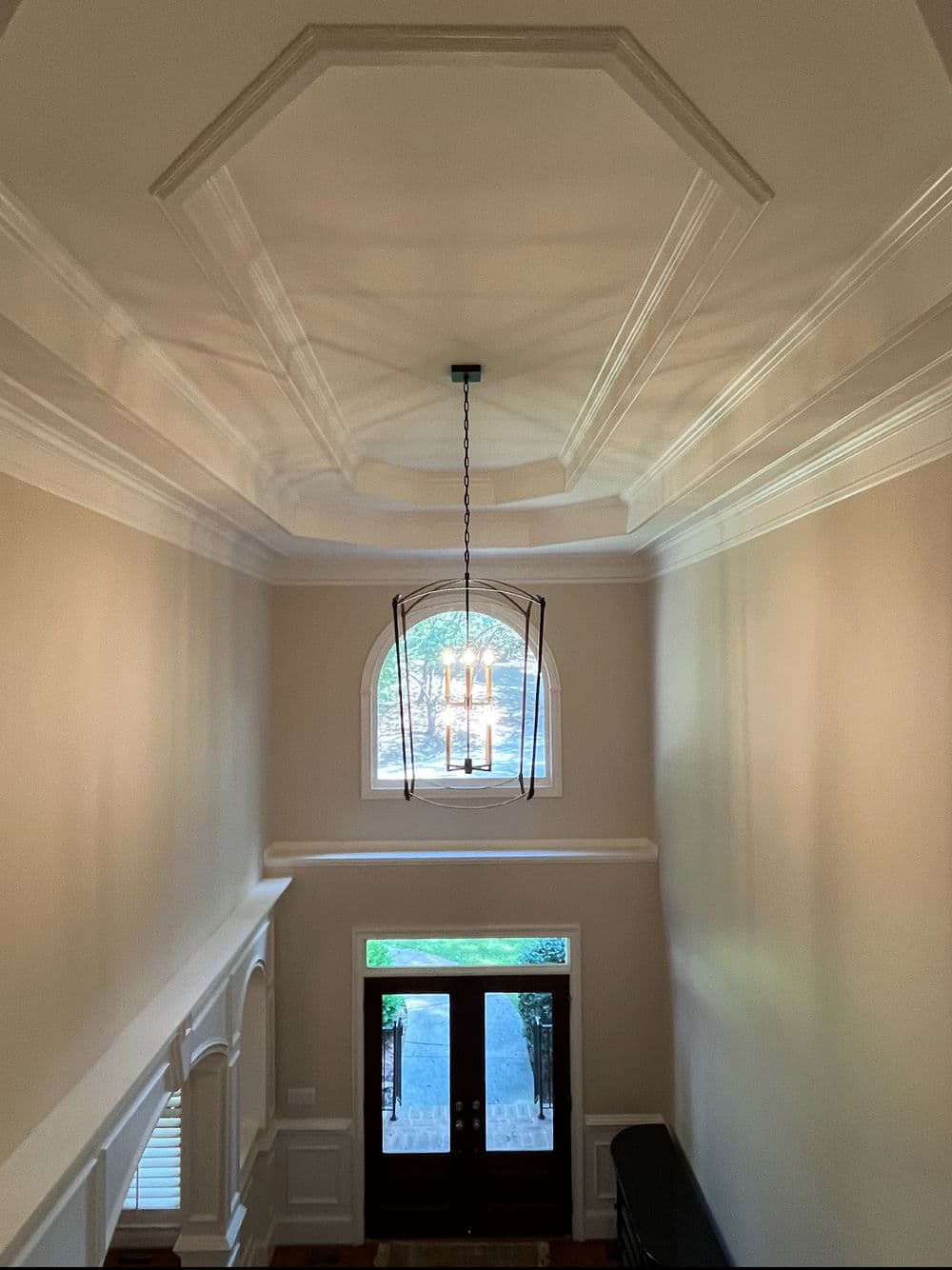 Elegant foyer with coffered ceiling, chandelier, and arched window, inviting natural light.