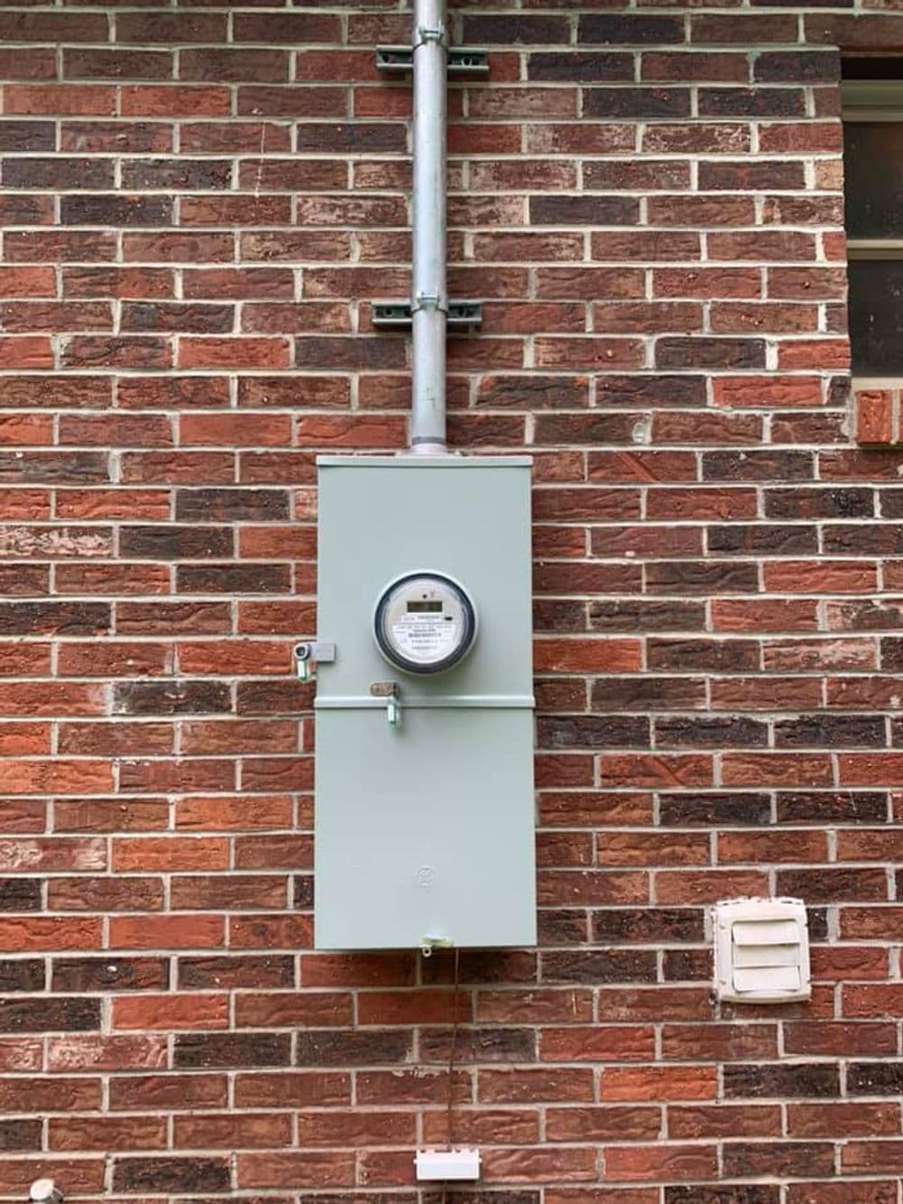 Electric meter mounted on a brick wall, with conduit and meter reading visible.