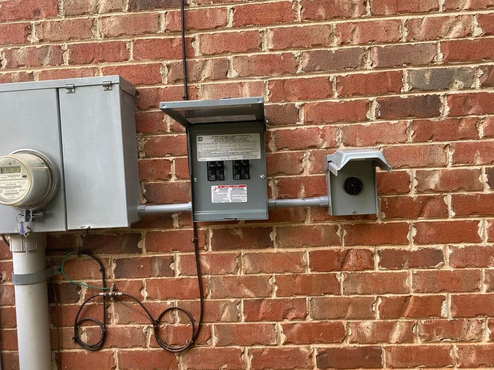 Electric meter and breaker box mounted on a brick wall with external outlet.