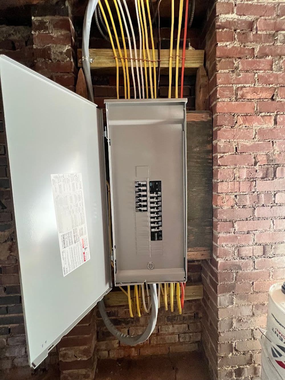 Electrical panel with open access, displaying circuits and connected wires in a brick wall setting.