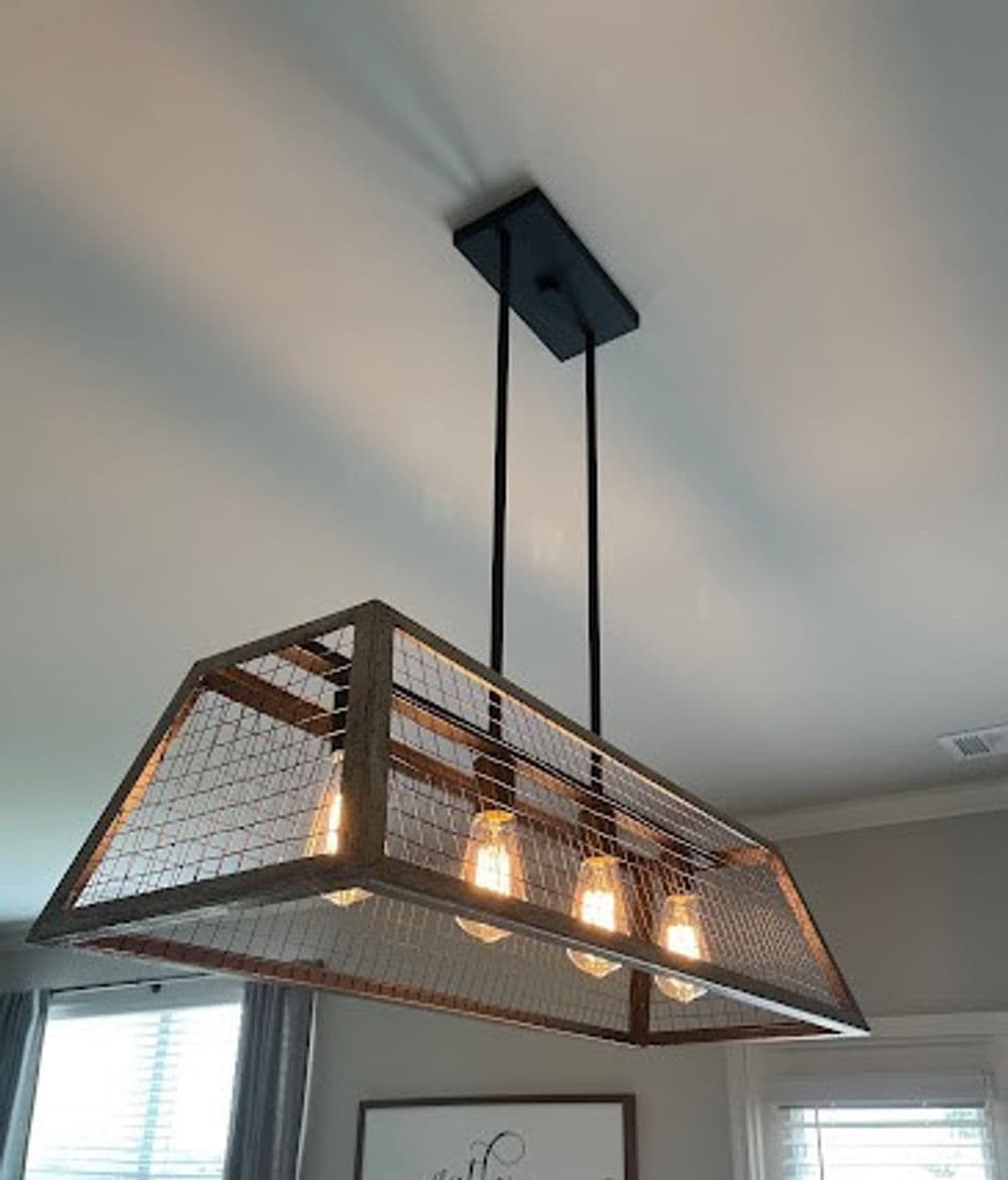 Industrial ceiling light fixture with four bulbs and a wire mesh design, suspended from a black mount.