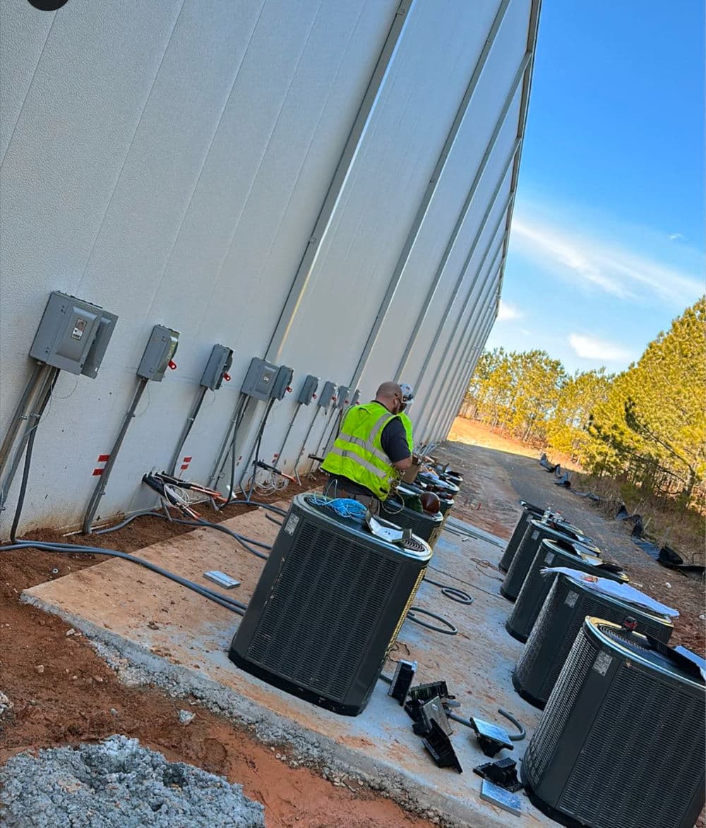 Technician working on HVAC units outside a building on a sunny day.