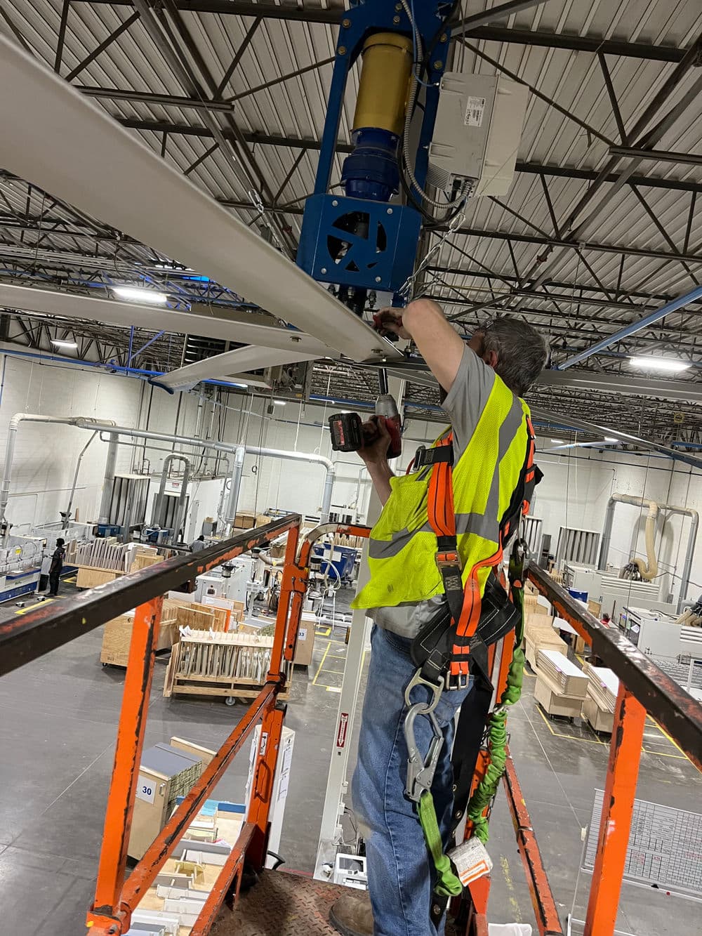 Worker in safety gear operating a drill on a lift in a warehouse setting.