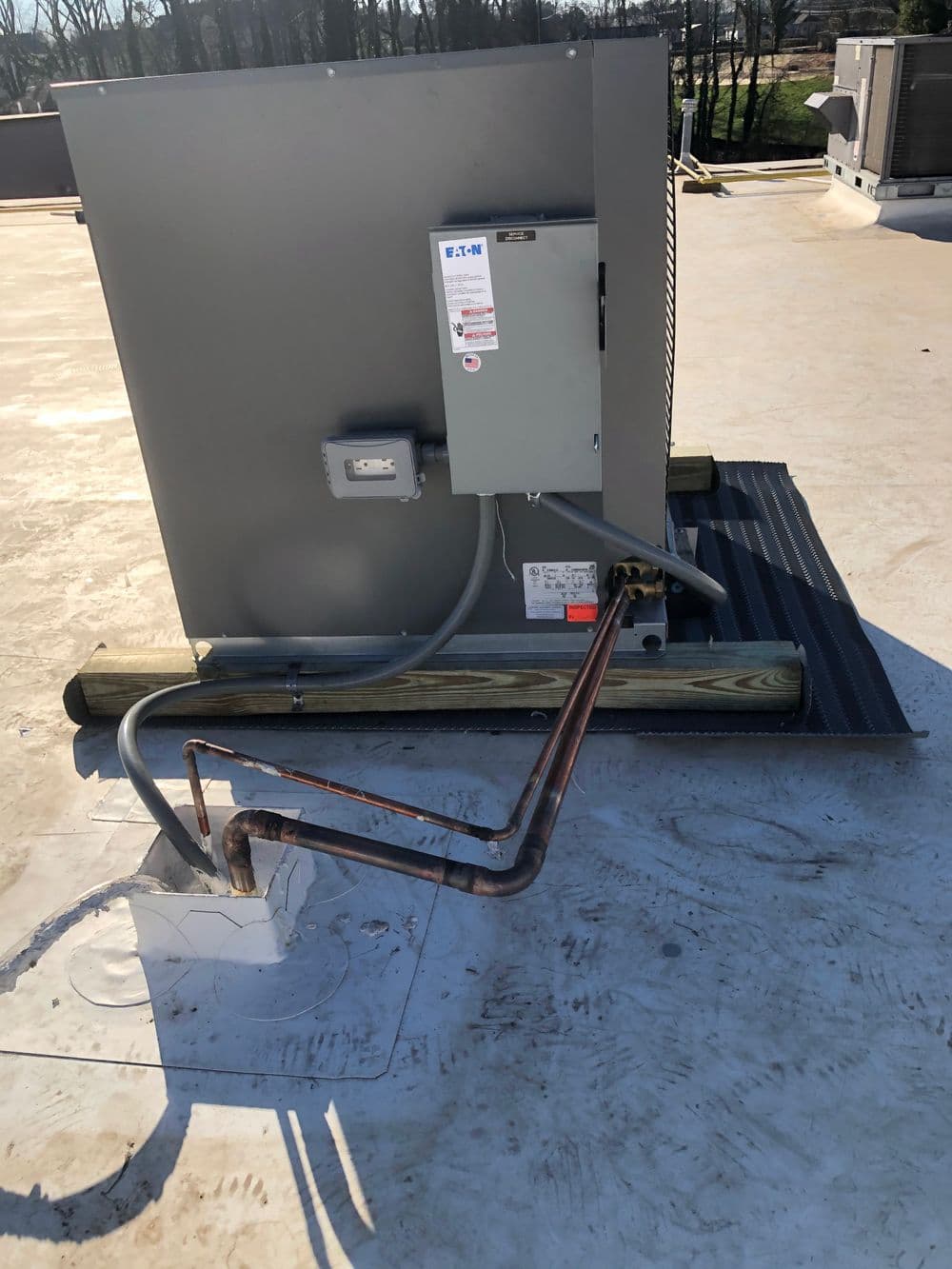 Rooftop HVAC unit with copper piping and electrical panel against a clear sky background.