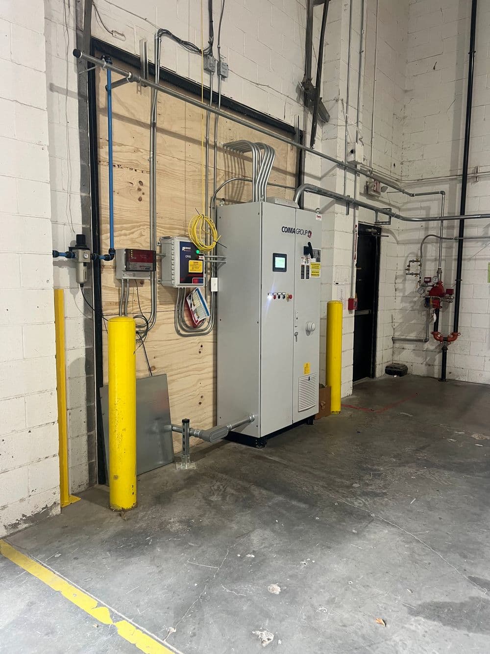 Industrial electrical control panel setup in a warehouse with safety barriers and electrical lines.