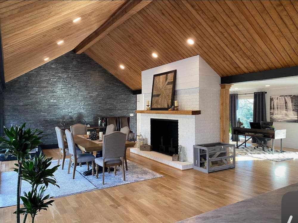 Modern living room with wooden beams, stone wall, dining table, and cozy fireplace.