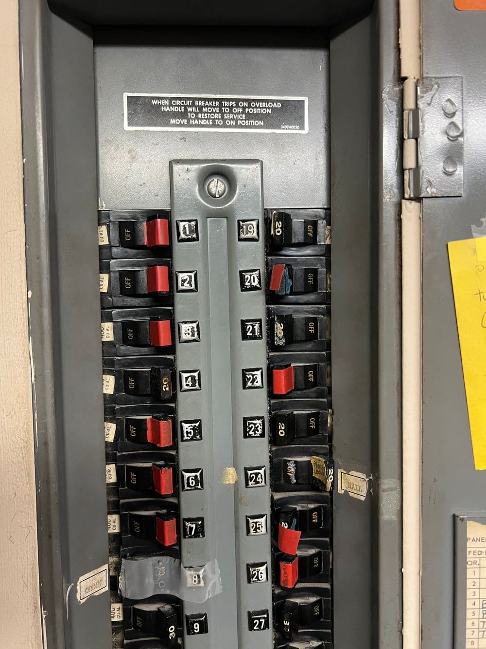 Electrical circuit breaker panel with labeled switches, warning notice on overload.